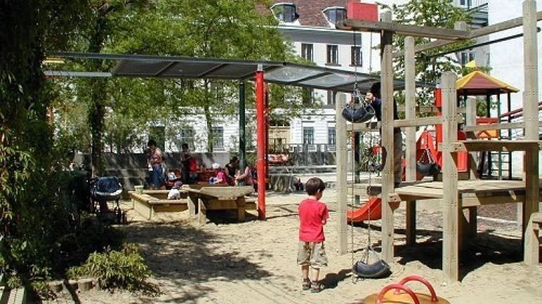 Kinder spielen auf Sandspielplatz mit Federwippe und Kletterturm