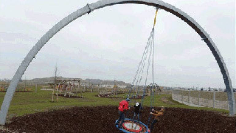 3 Personen schwingen auf einer Scheibe, die an einem großen Metallbogen hängt