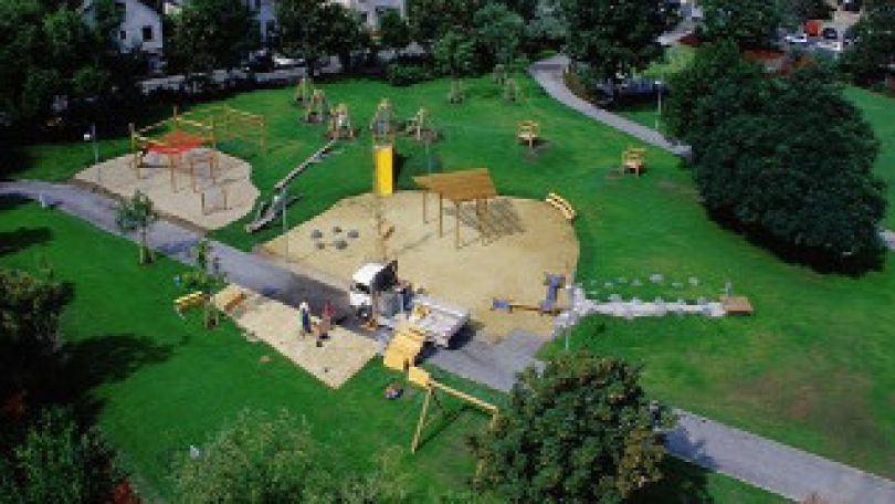 Blick von oben auf den Park mit Spielplatz, einer Sandfläche, Rasen und Bäumen
