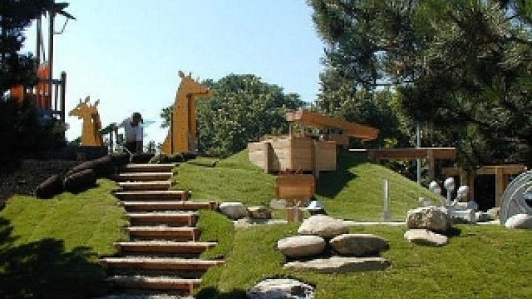 Holzstufen in grünen Hügel, oben Holzgiraffen und ein Holzwasserspiel