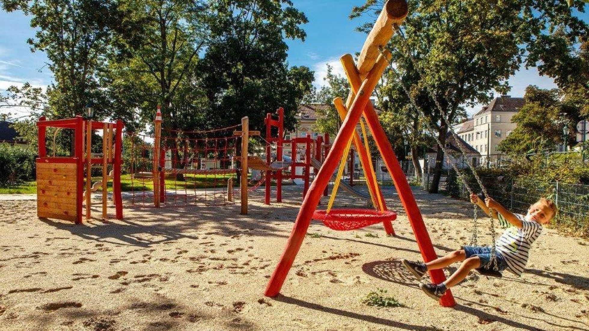 copyright: Wiener Stadtgärten/Houdek Spielplatz mit roter Nestschaukel, Klettergerüst und weiteren Spielgeräten