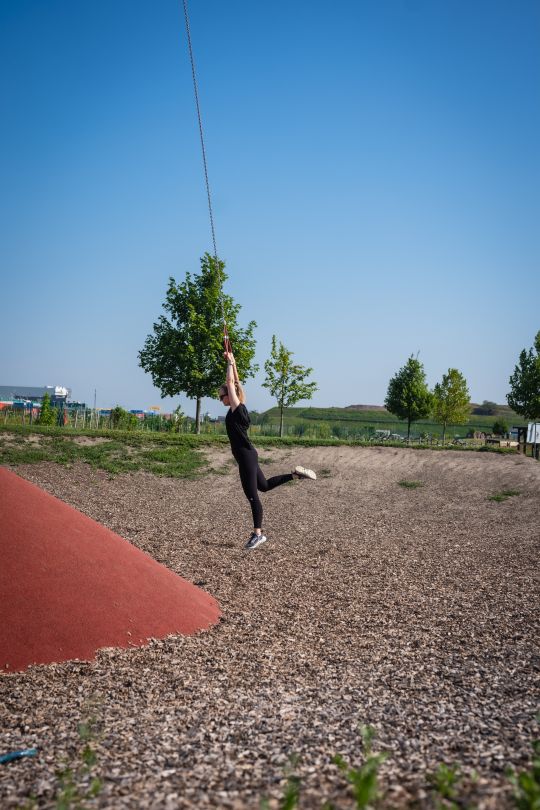 Eine Person schwingt an einem Seil, das an einer großen Metallstange hängt