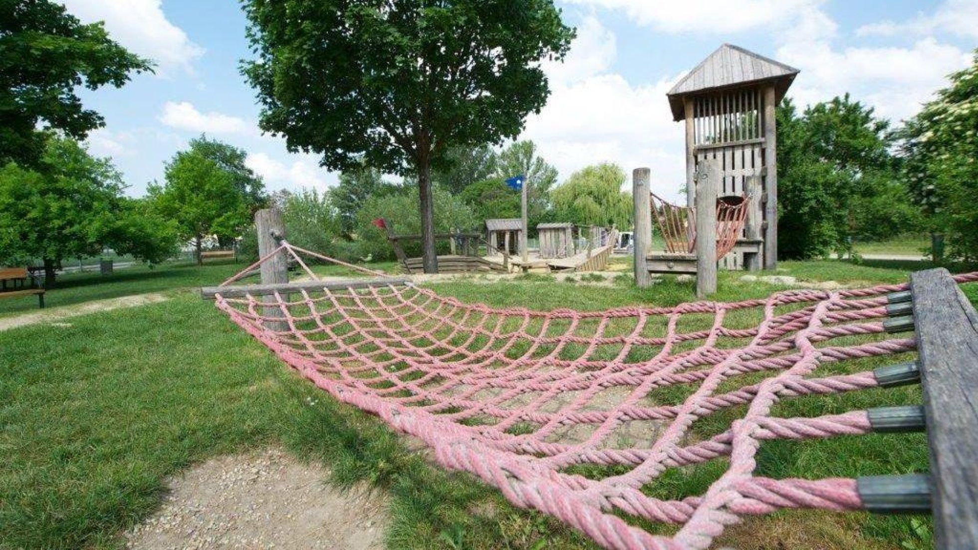 Hängematte, dahinter Klettergerüst und Spielgeräte aus Holz in einem Park