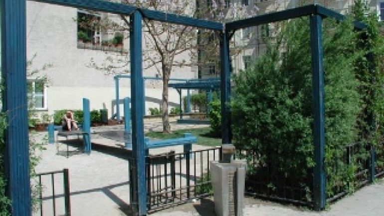 Parkeingang mit modernem Trinkbrunnen, blauer Pergola und einem niedrigen Zaun