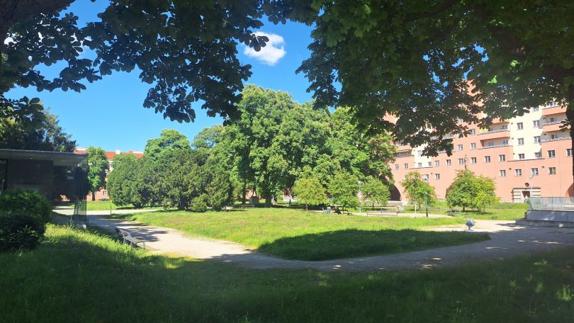 Grünfläche, Wege und Bäume, dahinter ein Gebäude
