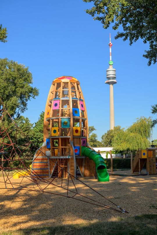 Klettergerüst mit Rusche in Form einer Rakete, dahinter der Donauturm