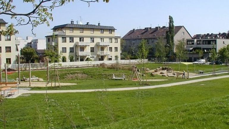 Sandspielplatz und Kletterwald in Rasenmulde, dahinter sind Häuser
