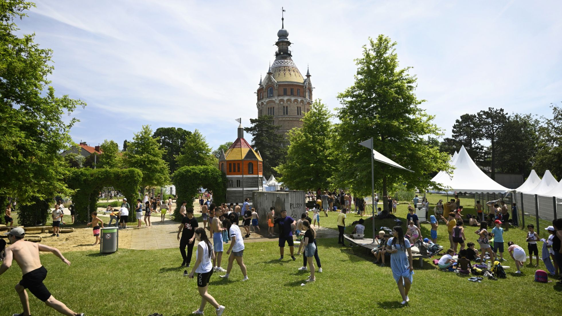 Grüne Wiese mit Menschen, im Hintergrund Wasserturm