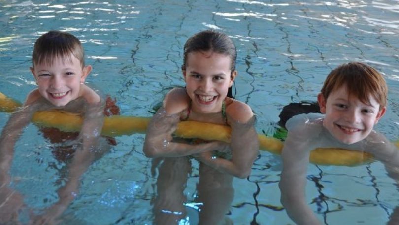 Kinder schwimmen mit einer Schwimmnudel im Wasser