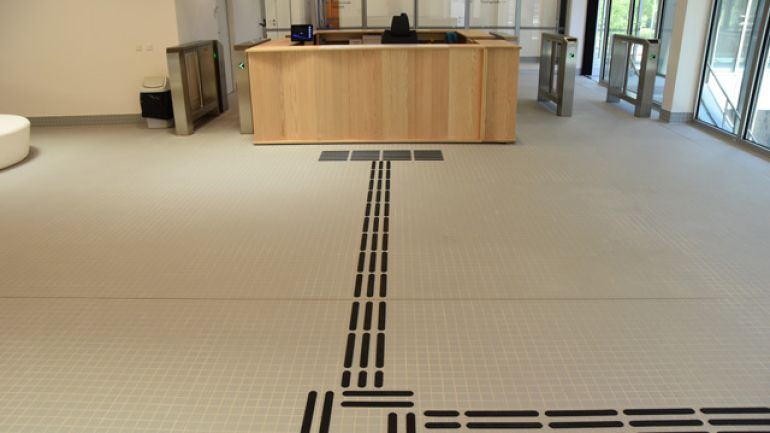 Bodenleitsystem, das zur Kassa führt. Links und rechts von der Kassa sind breite Durchgänge Richtung Schwimmhalle