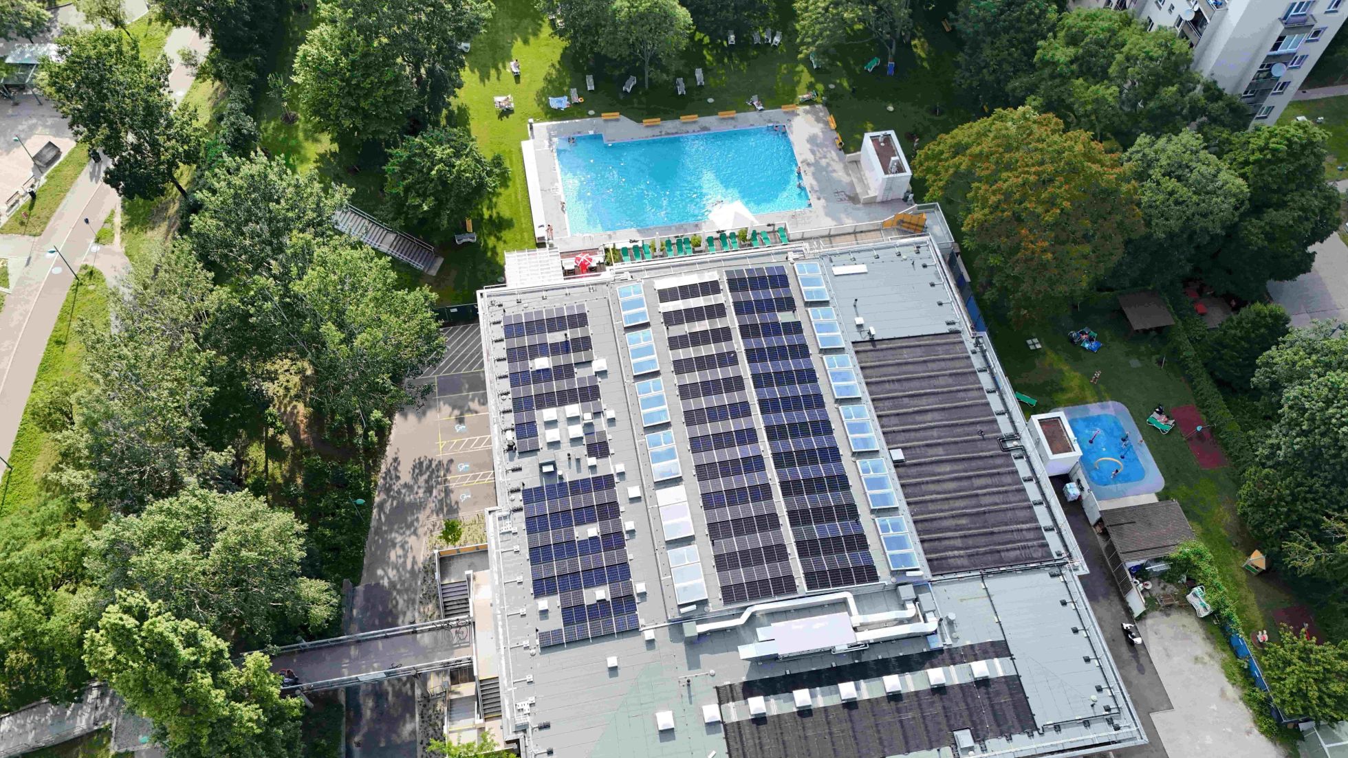 Photovoltaik-Anlage am Dach, 1 großes und ein kleines Außenbecken, rund ums Gebäude stehen einige Bäume.