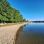 Flacher Badestrand an der Alten Donau. Auf der Liegewiese spenden große Bäume Schatten.