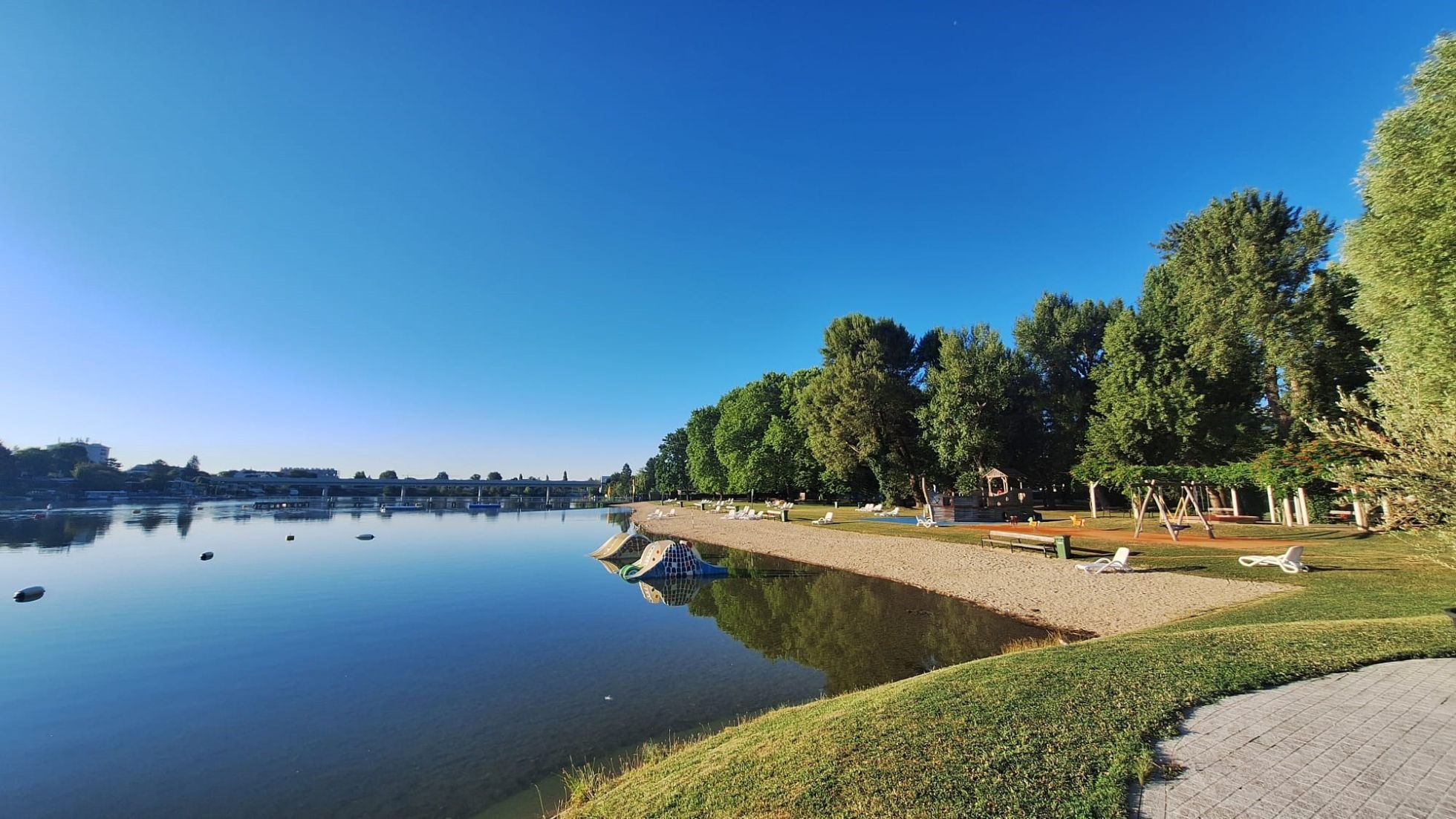 Liegewiese und Badestrand an der Alten Donau. Im flachen Wasser stehen 2 Kinderrutschen.