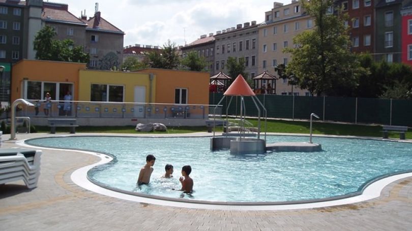 Kinderbecken im Freien mit Rutsche und badenden Menschen