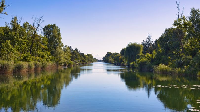Im ruhigen Gewässer spiegeln sich der Himmel und die Bäume, die links und rechts am Ufer stehen.