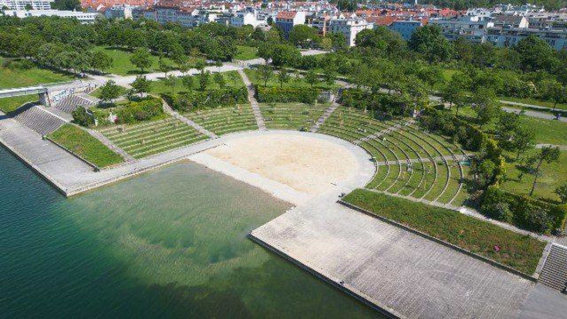 Blick von oben auf den Arena Beach: Halbrunde Liegewiesen, in der Mitte ein Sandstrand mit flachem Zugang zur Neuen Donau.