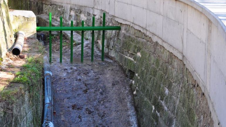 Bach fließt durch ein Metallgitter