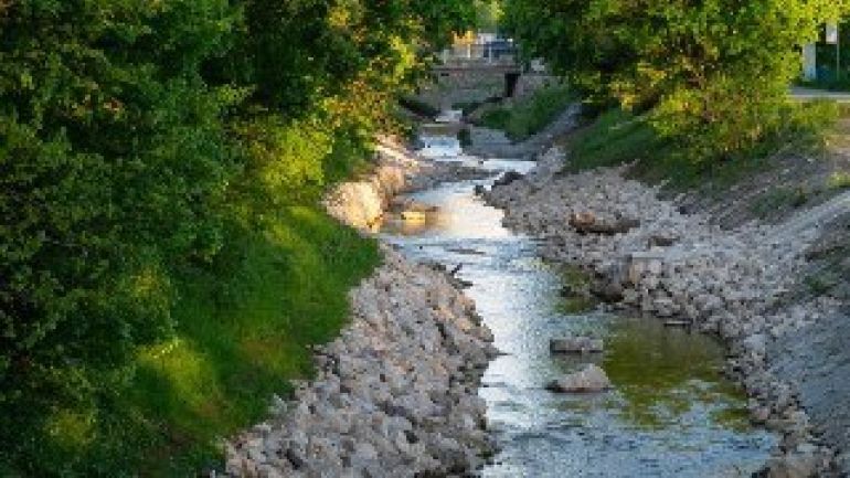 copyright: Wiener Wildnis Renaturiertes Bachbett des Liesingbaches. An beiden Ufern mit hellen Steinschüttungen, die in frühsommerlich grüne Böschungen übergehen