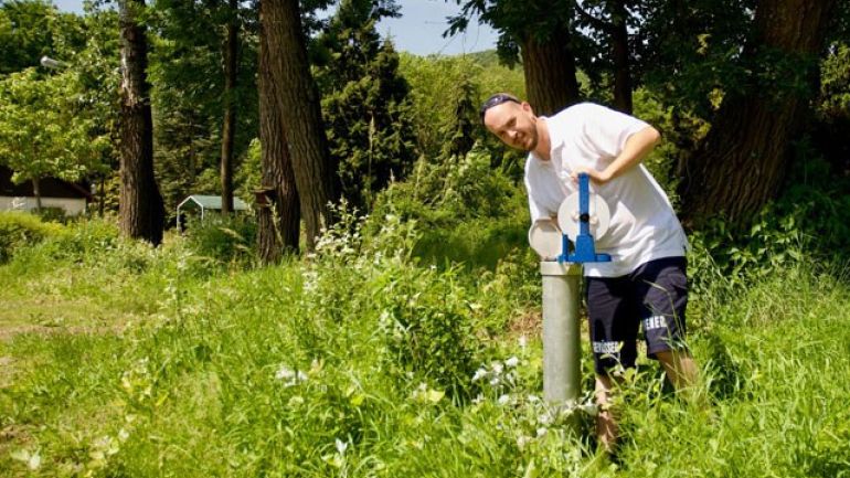 Mitarbeiter misst Grundwasserstand inmitten von Wiesen und Bäumen