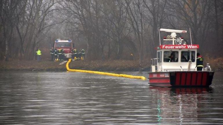 Ein Boot der Berufsfeuerwehr zieht eine gelbe Ölsperre ins Wasser.