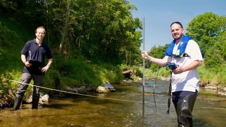 Zwei Mitarbiter stehen in Bach zur Abflussmessung