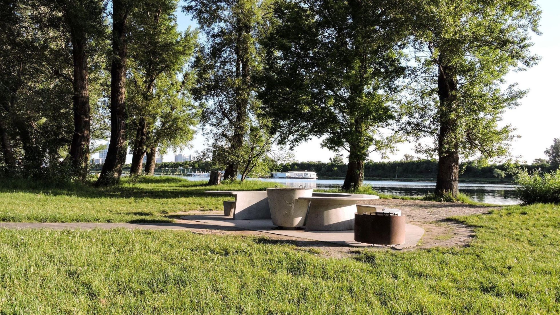 copyright: Wiener Gewässer Grillplatz mit Tisch und Sitzelementen aus Beton inmitten von Wiese auf der Wiener Donauinsel