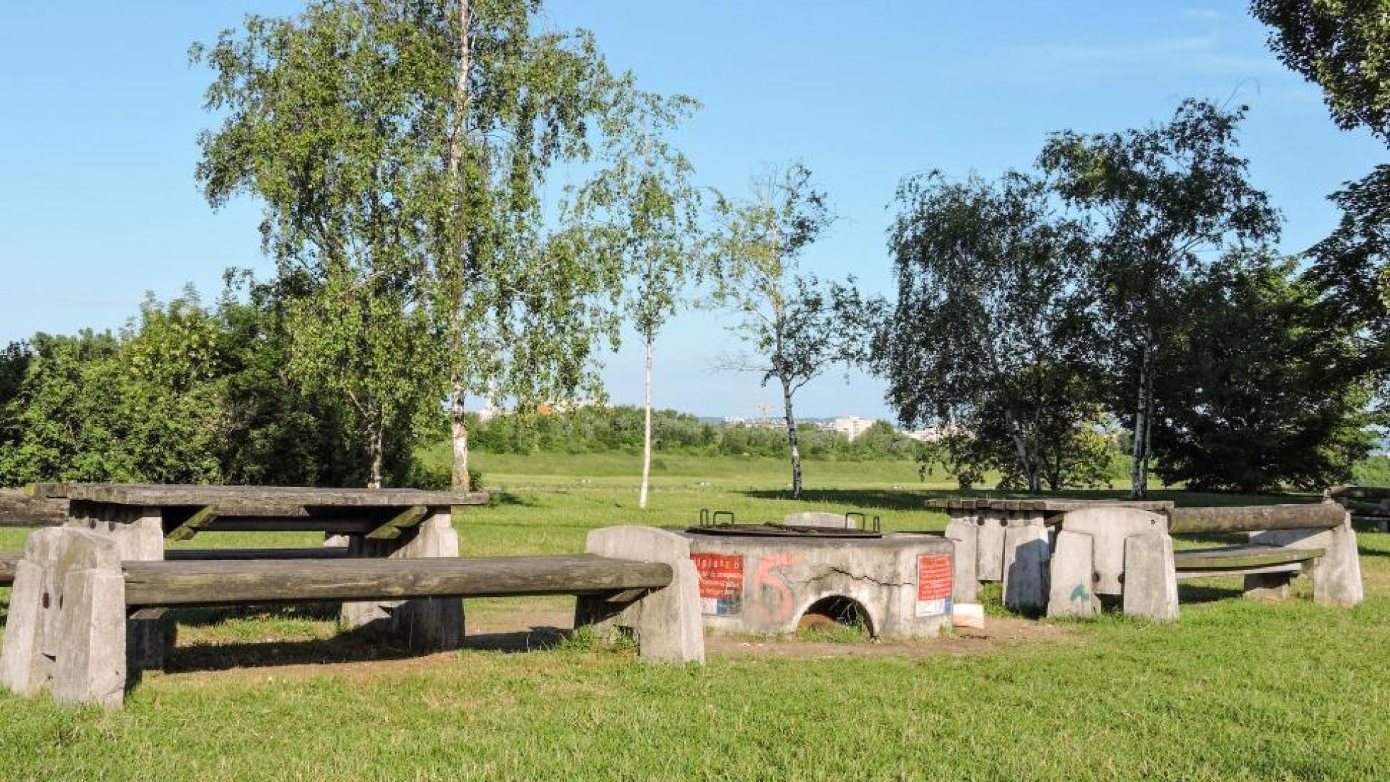 Grillplatz mit Sitzgelegenheiten, rund herum Wiese und Bäume