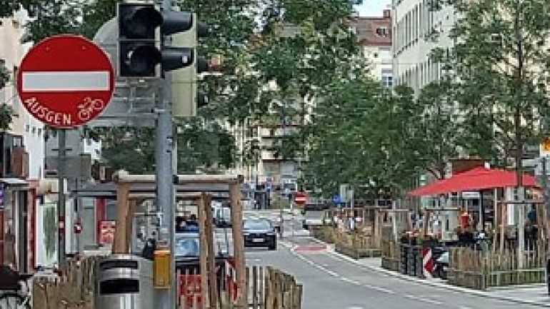 Links von der Fahrbahn steht ein Verkehrsschild "Einfahrt verboten ausgenommen Radfahrer". Ein Auto fährt iin der Einbahnstraße.
