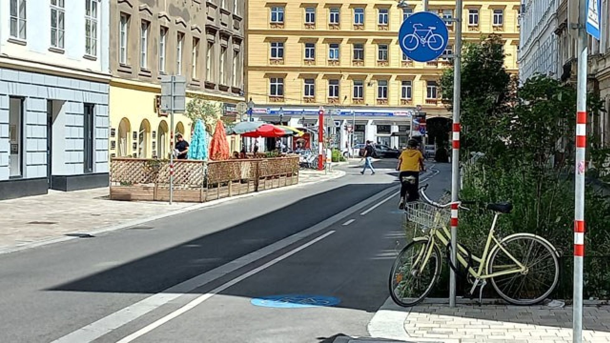 Ein Radweg verläuft zwischen Gehsteig und Fahrbahn. Der Radweg ist mit einem Verkehrszeichen und einer Piktogramm am Boden gekennzeichnet.