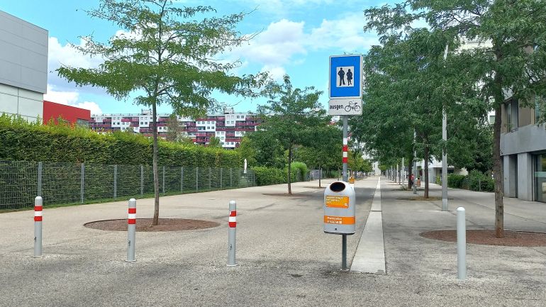 copyright: MA 46 Ein Schild "Fußgängerzone ausgenommen Fahrräder" steht an einer Straße. Absperrpfosten blockieren die Zufahrt für große Fahrzeuge.