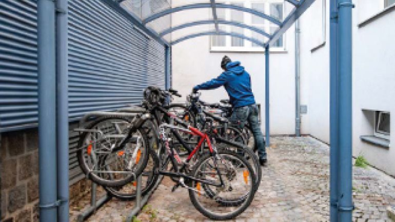 Mann schiebt sein Rad in eine überdachte Radabstellanlage