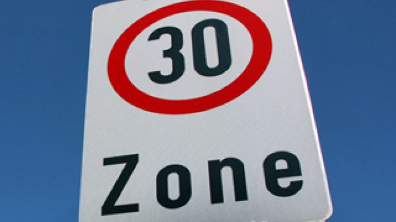 Hinweisschild "Tempo-30-Zone"; weiße Tafel mit schwarzer Zahl "30" in rot-umrandetem Kreis, darunter schwarze Schrift "Zone"