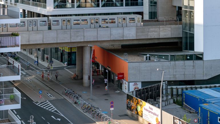 Neben einer Straße sind Fahrradabstellplätze. Über der Straße fährt eine U-Bahn.