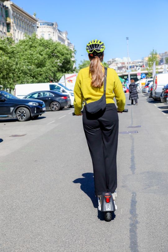 Frau mit Helm fährt mit E-Roller auf einer Straße.