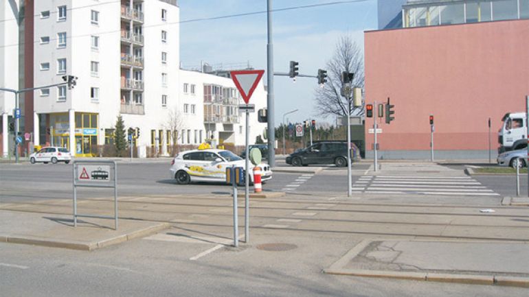 Kreuzungsbereich Anton-Schall-Gasse - Brünner Straße: breite Kreuzung mit Straßenbahnschienen, Fußgängerinseln, Zebrastreifen und Fußgängerampel