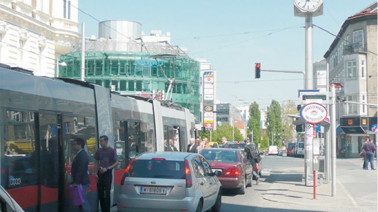 copyright: AUVA Straßenbahn in Haltestelle, Autos stehen direkt neben Straßenbahn, in die Fahrgäste aus- und einsteigen