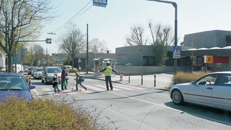 Kreuzungsbereich Grinzinger Straße - Bereich Schule: Straße mit rot unterlegtem Zebrastreifen und einem Schülerlotsen