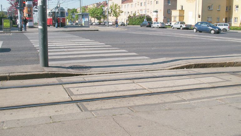 copyright: AUVA Kreuzungsbereich Neilreichgasse - Raxstraße: Breite Straßenkreuzung mit Straßenbahnschienen und Verkehrsinseln, Zebrastreifen und Fußgängerampel