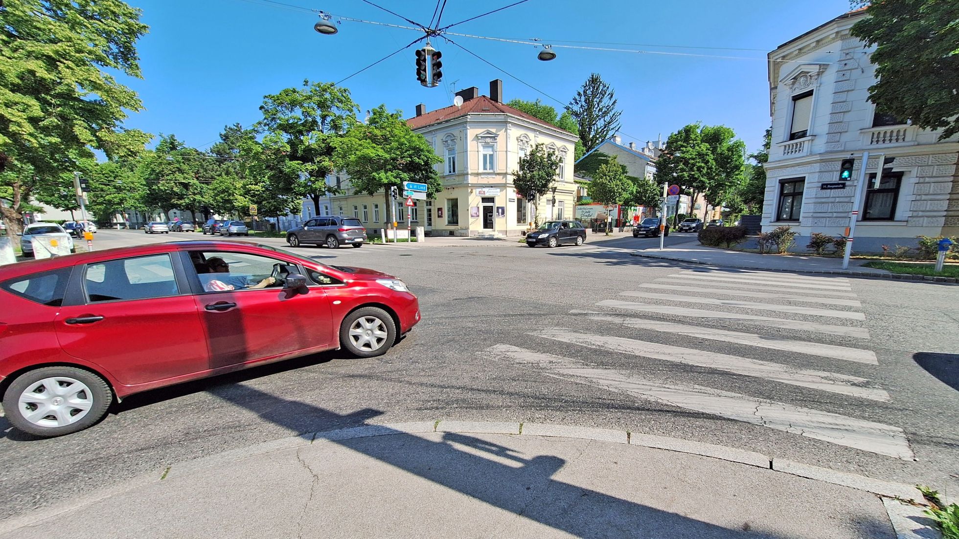 copyright: AUVA Ein rotes Auto biegt rechts ab, die Fußgänger-Ampel mit Zebrastreifen zeigt grün