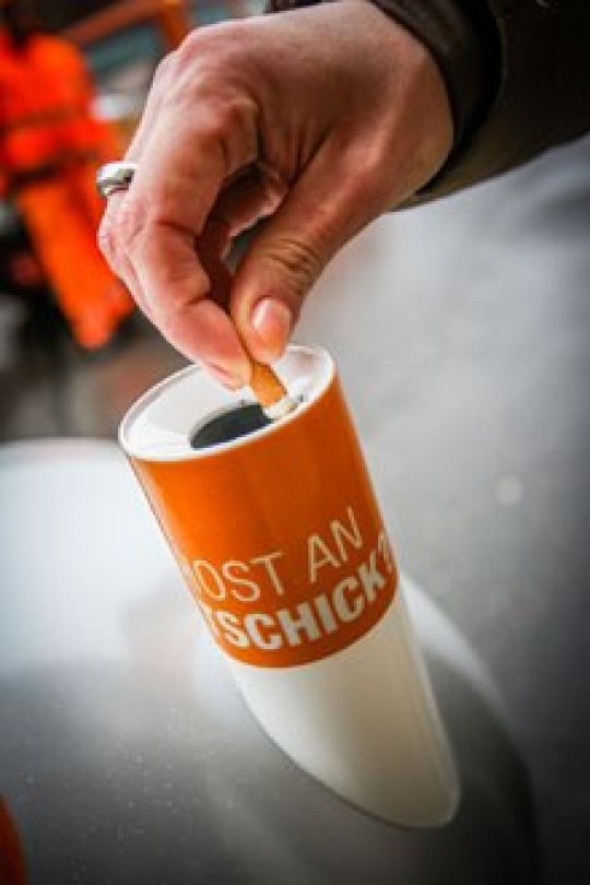 Person wirft einen Zigarettenstummel in ein Aschenrohr