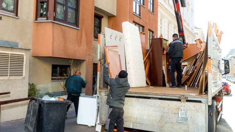 3 Personen stehen an einem offenen Umzugswagen vor einem Gebäude und laden Möbel ein.