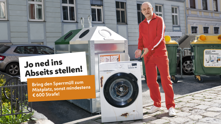 copyright: Philipp Horak Herbert Prohaska in einem roten Trainingsanzug neben einer Waschmaschine, links eine weiße Box mit dem Schriftzug "Jo ned ins Abseits stellen", darunter eine orange Box mit dem Schriftzug "Bring den Sperrmüll zum Mistplatz, sonst mindestens € 600 Strafe!"