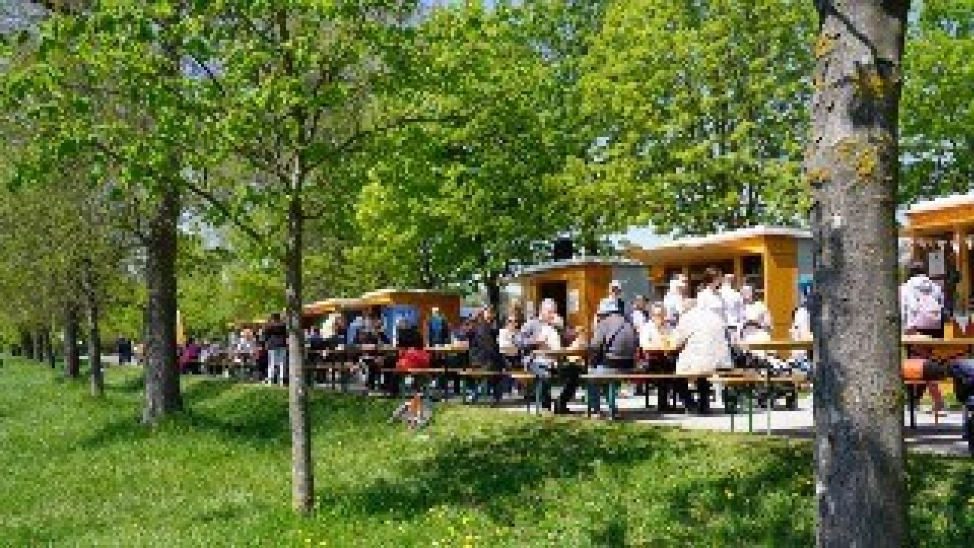 Leute sitzen im Grünen vor Verkaufsständen auf Bierbänken
