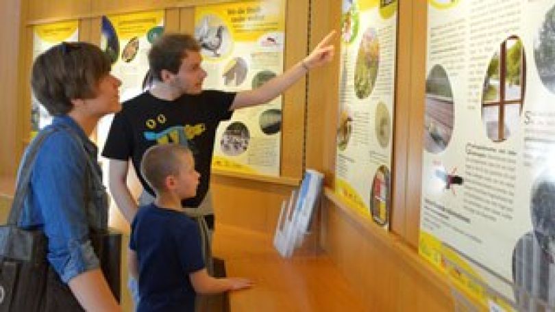 Ein Mann zeigt einer Frau und einem Kind etwas auf einer Informationstafel.