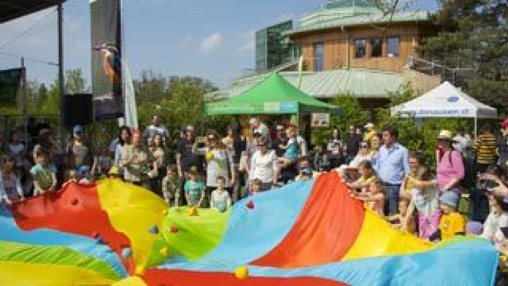 Kinder und Erwachsen spannen ein großes buntes Tuch auf