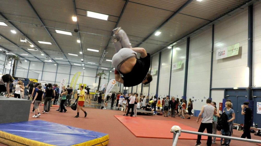 Ein Jugendlicher macht einen Salto in einer Sport und Fun Halle; dahinter weitere Personen, die Sport machen.