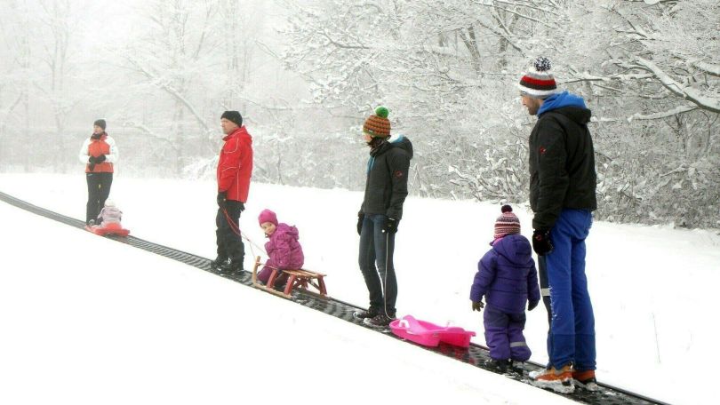 Kinder und Eltern mit Bobs und Schlitten auf einem Schlitten-Förderband