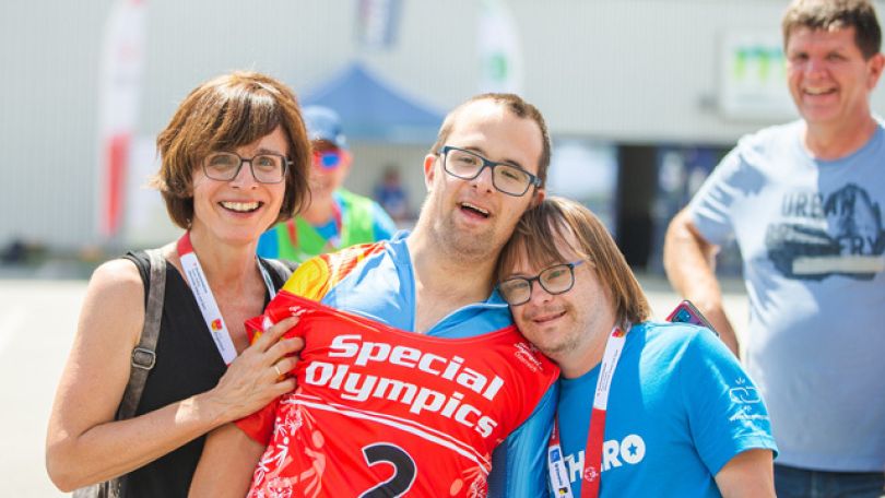 copyright: GEPA pictures 2 junge Männer mit einem Special-Olympics-Trikot und einer Medaille sowie eine Frau lehnen sich aneinander an und lächeln in die Kamera. Im Hintergrund steht ein weiterer Mann in Freizeitkleidung.