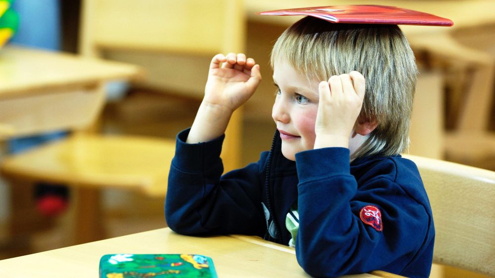 copyright: Bilderbox.com Ein Bub in einem Klassenzimmer balanciert ein Heft auf dem Kopf.