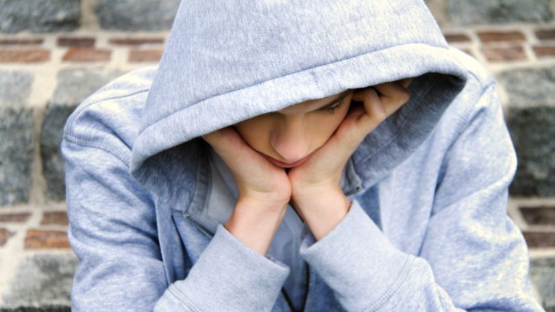 Junger Mann, der den Kopf in die Hände stützt und zu Boden blickt